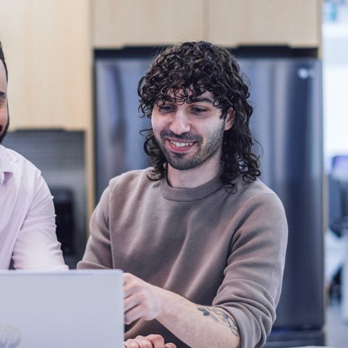An employee beside their coworker looking at a laptop