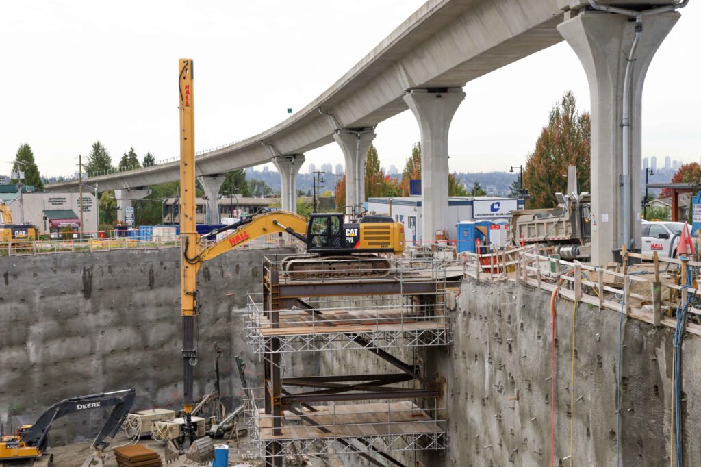 A hall construction crane in a pit below the sky train line