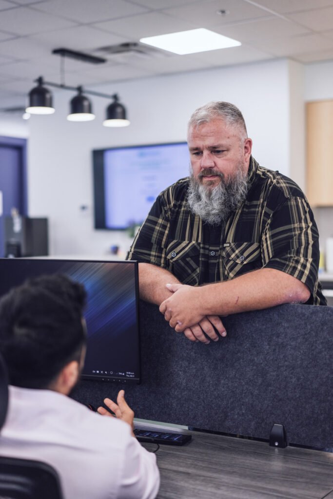 A coworker stands at anothers desk talking